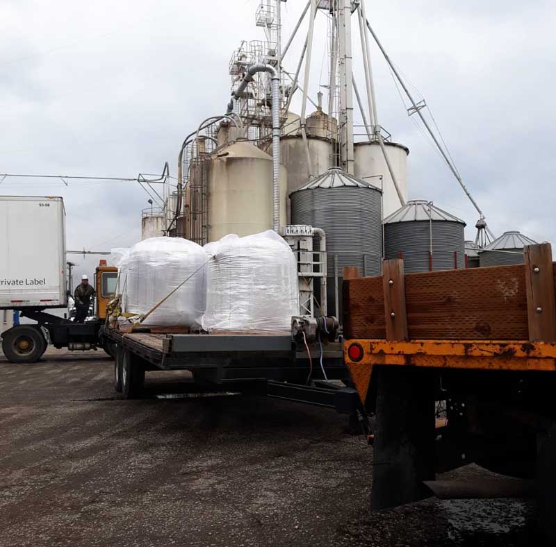 a trailer full of super-sacks of malt in front of several large grain bins